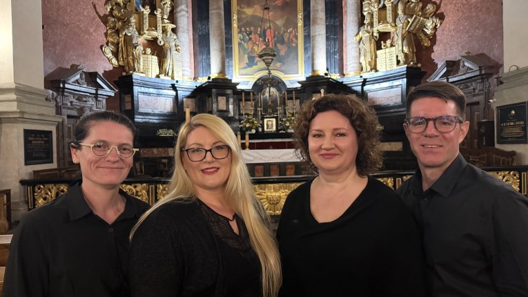 Czwórka wykonawców na tle ołtarza kościoła.