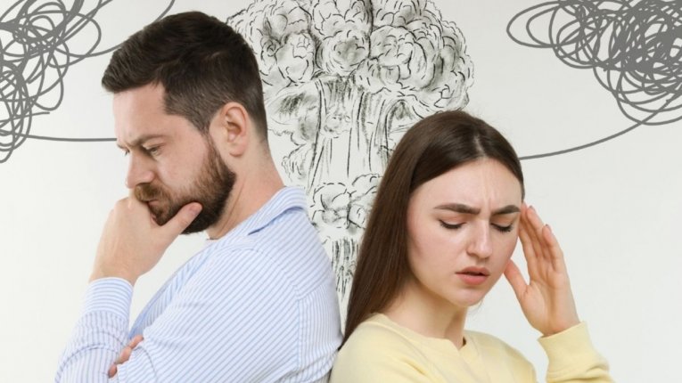 Kobieta i mężczyzna stoją do siebie plecami z wyraźnym grymasem napięcia i smutku na twarzach. Mężczyzna ma skrzyżowane ręce i dłoń przy brodzie, kobieta trzyma się za skroń, jakby miała ból głowy. Nad ich głowami narysowano czarne, splątane bazgroły symb