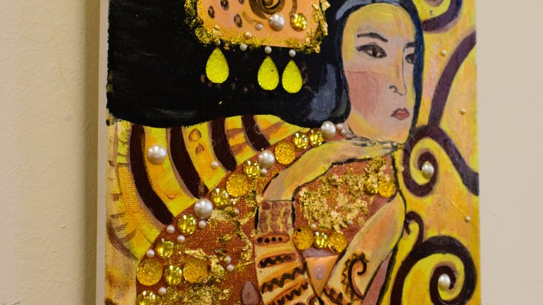Obraz w tonacji żółci i złota oraz beżu, brązu i czerni. Czarnowłosa kobieta patrząca w prawo. Jej ciało pokrywają ornamenty oraz perły i złote elementy, które autor przykleił do płótna.