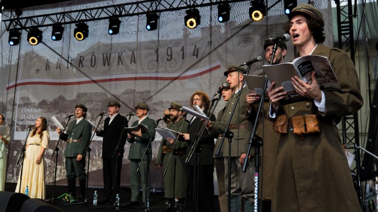 Artyści teatru Loch Camelot w strojach legionistów i dam śpiewaja pieśni patriotyczne